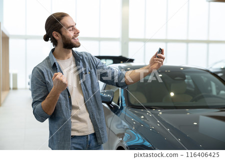Excited young bearded man in a car salon with car keys in hand Excited young bearded man in a car salon with car keys in hand 116406425