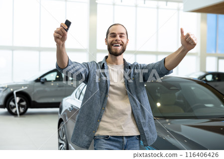 Excited young bearded man in a car salon with car keys in hand Excited young bearded man in a car salon with car keys in hand 116406426