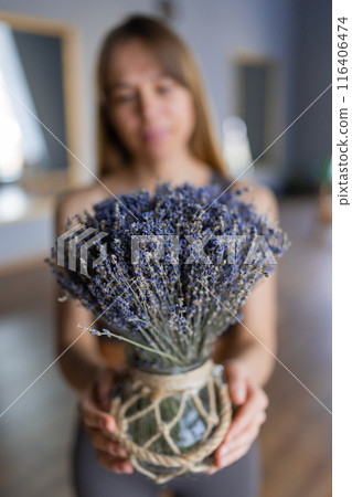 A serene woman holding a lavender bouquet in a rustic vase, embodying simplicity and natural beauty A serene woman holding a lavender bouquet in a rustic vase, embodying simplicity and natural beauty 116406474