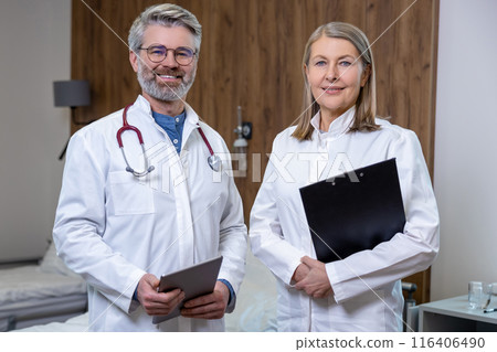 Two doctors standing in a room in clinic and looking positive Two doctors standing in a room in clinic and looking positive 116406490