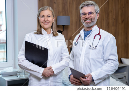 Two doctors standing in a room in clinic and looking positive Two doctors standing in a room in clinic and looking positive 116406491