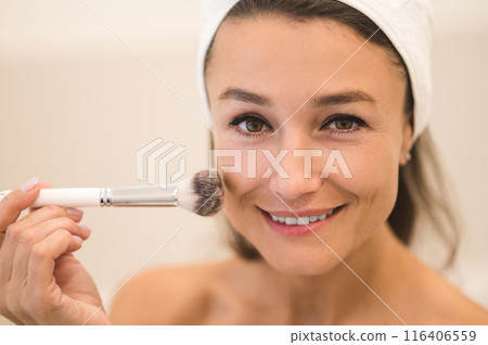Waist up of a woman doing make up and applying powder on her face Waist up of a woman doing make up and applying powder on her face 116406559