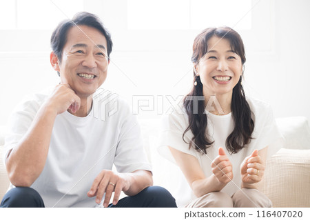 A smiling couple relaxing while watching fun TV in a bright room, front view 116407020
