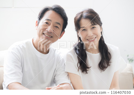 一對 50 多歲的中年夫婦在漂亮的背光客廳放鬆地看著鏡頭。 116407030