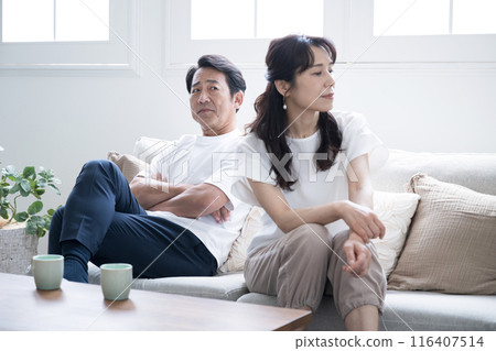 A couple in their 50s sitting on the sofa in a rut or quarrel. The image of a cold, unfriendly couple. A couple in their 50s sitting on the sofa in a rut or quarrel. The image of a cold, unfriendly couple. 116407514