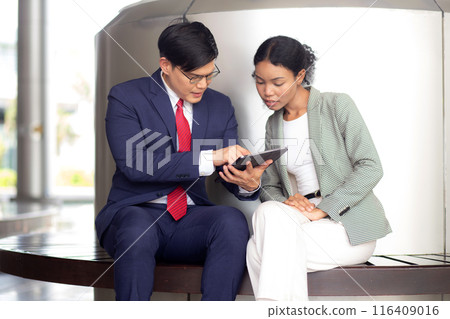 Two young business man and woman in formal meeting and discussing documents and using a tablet. Two young business man and woman in formal meeting and discussing documents and using a tablet. 116409016
