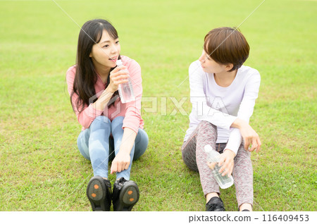Two women hydrating on the grass after exercise Two women hydrating on the grass after exercise 116409453