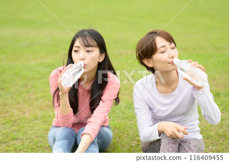 兩名女子運動後在草地上補充水分 116409455