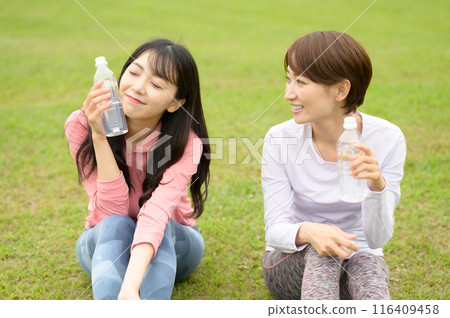 Two women hydrating on the grass after exercise Two women hydrating on the grass after exercise 116409458