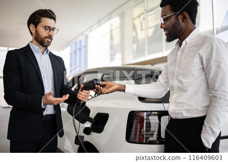Dealer demonstrates electric SUV charger to interested buyer in showroom Dealer demonstrates electric SUV charger to interested buyer in showroom 116409603