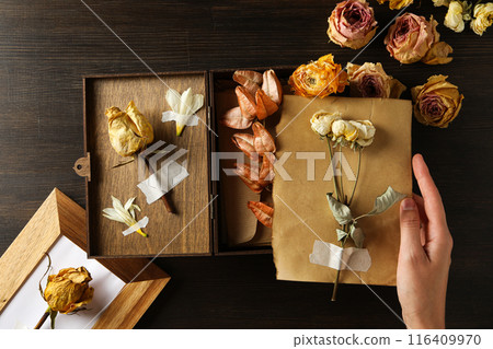 Dried flowers, wooden box, photo frame and envelope in hand on wooden background, top view Dried flowers, wooden box, photo frame and envelope in hand on wooden background, top view 116409970