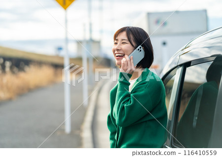 A woman calling in front of her car. A woman calling about car trouble. A woman calling in front of her car. A woman calling about car trouble. 116410559