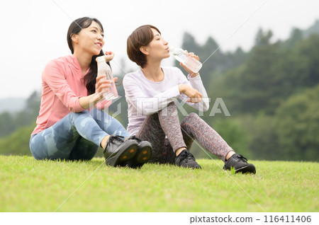 Two women hydrating on the grass after exercise 116411406