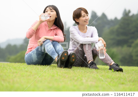 兩名女子運動後在草地上補充水分 兩名女子運動後在草地上補充水分 116411417