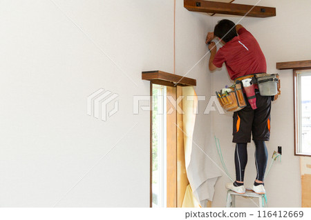 A craftsman applying wallpaper to a used house A craftsman applying wallpaper to a used house 116412669