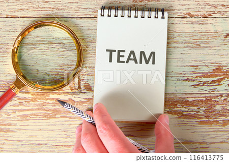 Learning English concept. TEAM word in a notebook that has a hand on the surface next to a magnifying glass Learning English concept. TEAM word in a notebook that has a hand on the surface next to a magnifying glass 116413775