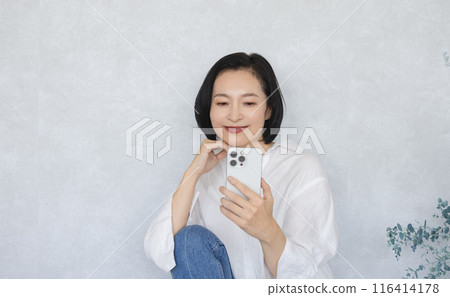 A smiling woman holding a smartphone A smiling woman holding a smartphone 116414178