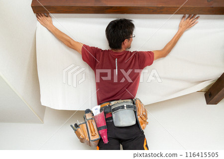 A craftsman applying wallpaper to a used house A craftsman applying wallpaper to a used house 116415505