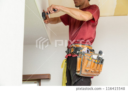 A craftsman applying wallpaper to a used house A craftsman applying wallpaper to a used house 116415548