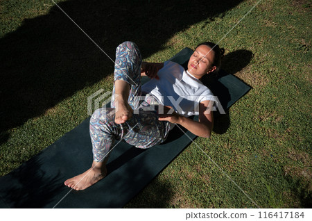 Woman practicing yoga outdoors in sunny park on exercise mat Woman practicing yoga outdoors in sunny park on exercise mat 116417184