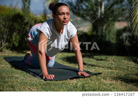 Woman practicing outdoor yoga poses on a mat in a serene natural setting 116417187