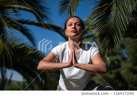 Woman practicing yoga outdoors in a peaceful environment surrounded by palm trees 116417240