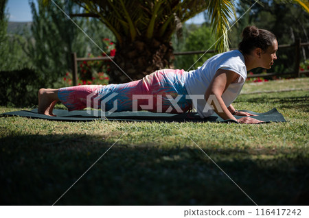 Woman practicing yoga outdoors on a sunny day in a peaceful garden setting 116417242