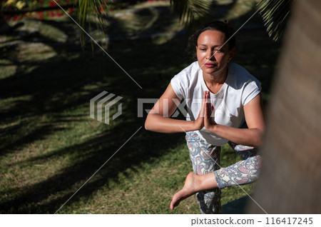 Woman practicing yoga outdoors in a peaceful park setting, displaying balance and concentration 116417245