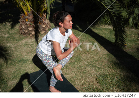 Woman practicing yoga poses outdoors in a garden, focusing on balance and concentration 116417247