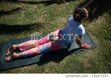 Woman practicing yoga outdoors on a sunny day performing the upward-facing dog pose 116417251