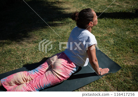 Woman practicing outdoor yoga in upward dog pose on a sunny day 116417256