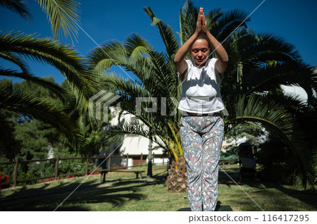 Woman practicing yoga outdoors in a peaceful park setting under bright sunlight Woman practicing yoga outdoors in a peaceful park setting under bright sunlight 116417295