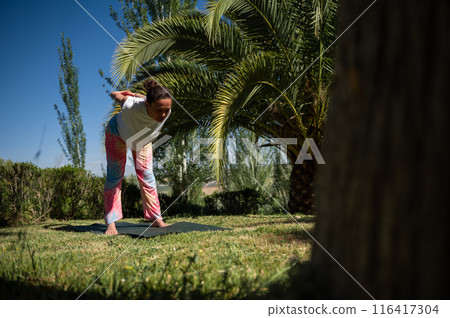 Woman practicing yoga in a serene outdoor setting with palm trees and lush greenery 116417304