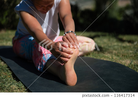 Woman stretching outdoors on a yoga mat on a sunny day, focusing on foot and leg stretch Woman stretching outdoors on a yoga mat on a sunny day, focusing on foot and leg stretch 116417314