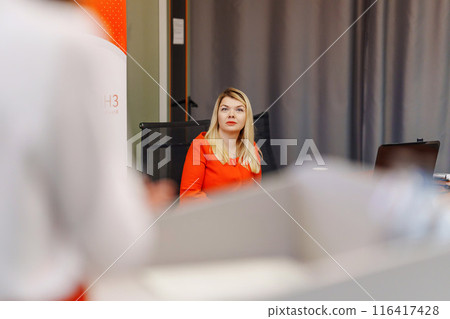 Attractive blonde woman in red dress listening to speaker at conference. Attractive blonde woman in red dress listening to speaker at conference. 116417428