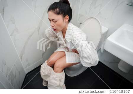 woman sitting on toilet bowl and holding her painful Stomach in bathroom 116418107