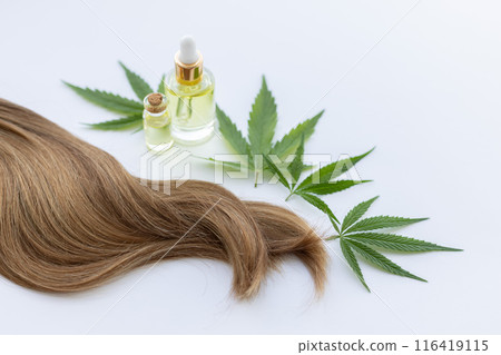 Strand of hair with small bottles of cannabis oil and fresh green cannabis leaves.  116419115