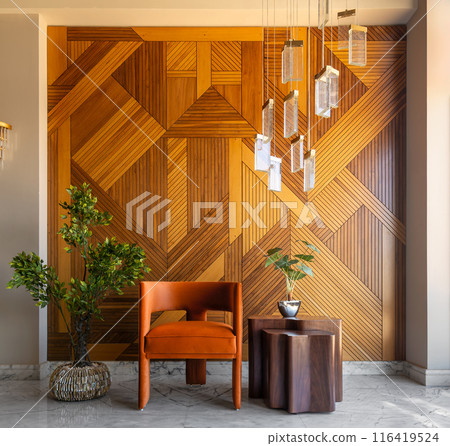 Modern orange chair and coffee table against wood wall with lights and potted plant 116419524