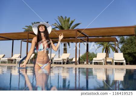 Brunette woman in white hat relaxing at the pool during vacation 116419525
