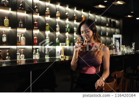 Gorgeous young woman enjoying glass of whiskey at nightclub in the city Gorgeous young woman enjoying glass of whiskey at nightclub in the city 116420164