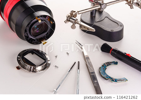 A broken lens of a professional camera and repair tools on a white table.  116421262