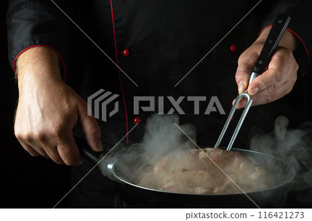 Chef turns sausage with fork in hand while frying it in a frying pan. Concept of cooking sausage in hotel kitchen Chef turns sausage with fork in hand while frying it in a frying pan. Concept of cooking sausage in hotel kitchen 116421273