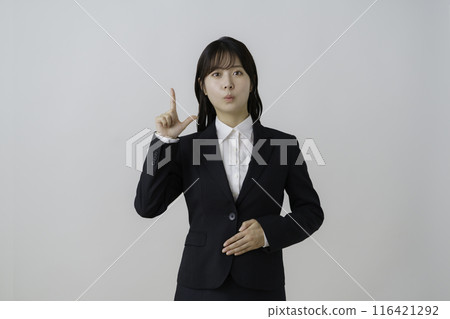 一位年輕女子在白色背景下穿著西裝用手指擺姿勢的肖像 一位年輕女子在白色背景下穿著西裝用手指擺姿勢的肖像 116421292