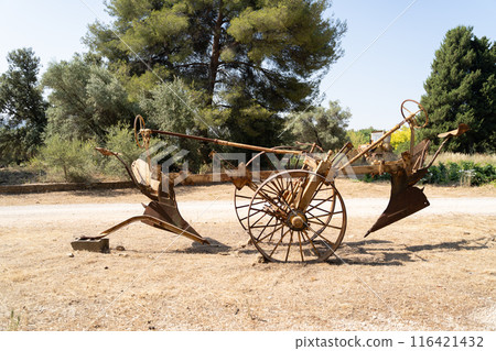 A vintage rusty farm plow with old wooden wheels in a rustic rural setting 116421432