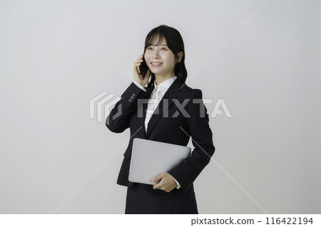 Portrait of a young woman wearing a suit and holding a laptop and smartphone on a white background Portrait of a young woman wearing a suit and holding a laptop and smartphone on a white background 116422194