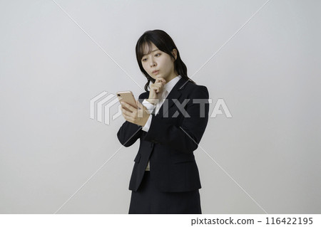 Portrait of a young woman wearing a suit and thinking with a smartphone in her hand against a white background Portrait of a young woman wearing a suit and thinking with a smartphone in her hand against a white background 116422195