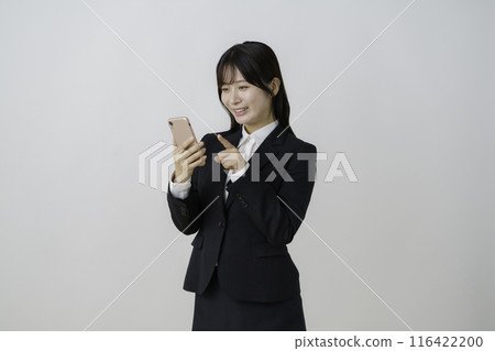 Portrait of a young woman wearing a suit and clicking a smartphone on a white background Portrait of a young woman wearing a suit and clicking a smartphone on a white background 116422200