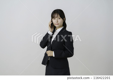 Portrait of a young woman wearing a suit and talking on a smartphone against a white background 116422201