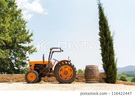 Vintage orange tractor near a barrel and tree in the tranquil countryside 116422447