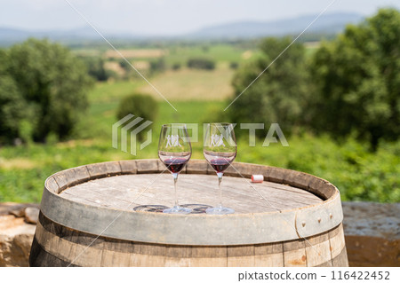 Wine glasses arranged on a barrel overlooking a scenic vineyard landscape 116422452